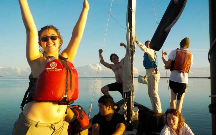 a group of students raise their hands in success on a sailboat in florida